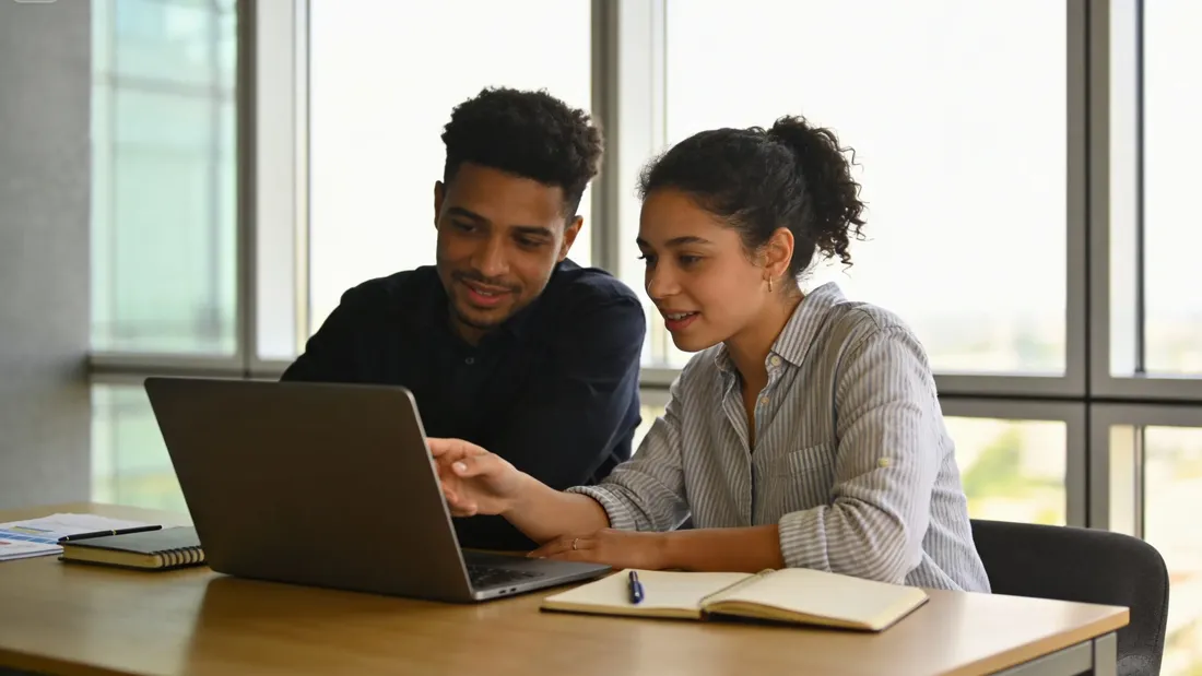 Deux personnes analysent un budget sur un ordinateur portable, avec un carnet et des documents