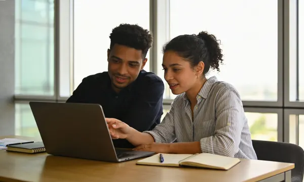 Deux personnes analysent un budget sur un ordinateur portable, avec un carnet et des documents
